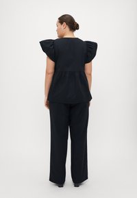 Black top with puff sleeves, peplum waist, and a smooth texture, paired with loose-fitting black trousers. Simple and elegant design.