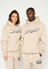 Felpe beige con logo stampato in nero, dotate di tasche a marsupio e polsini a costine, abbinate a pantaloni della tuta coordinati decorati con accenti del logo.