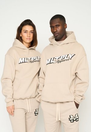 Beigen Kapuzenpullis mit einem schwarzen Logo-Druck, ausgestattet mit Kängurutaschen und gerippten Bündchen, kombiniert mit passenden Jogginghosen, die Logopunkte aufweisen.