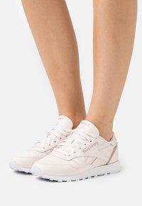 Reebok sneakers i mjuk rosa läder med vita detaljer. Funktioner inkluderar platta snörningar, perforerade detaljer och en vadderad plös för komfort.