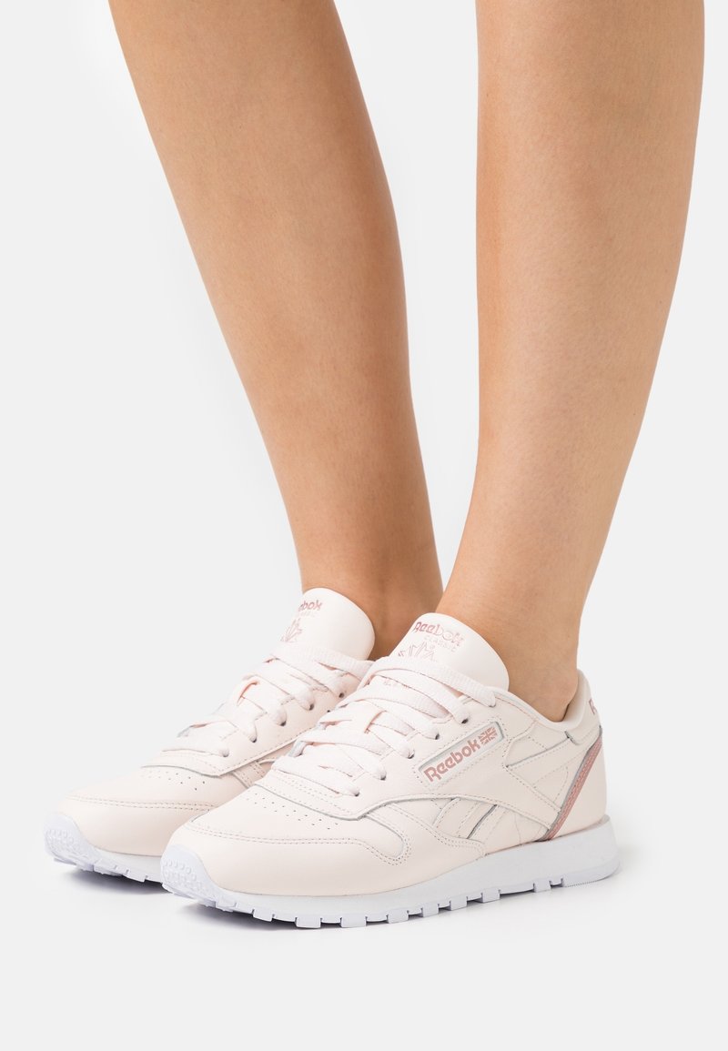 Reebok sneakers i mjuk rosa läder med vita detaljer. Funktioner inkluderar platta snörningar, perforerade detaljer och en vadderad plös för komfort.