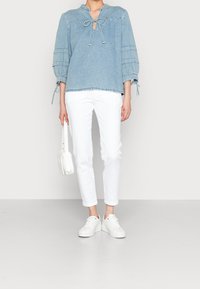 Ljusblå denimblus med nyckelhålsringning och knytdetalj, med långa, insamlade ärmar. Kombinerad med vita slim fit-byxor och vita sneakers.