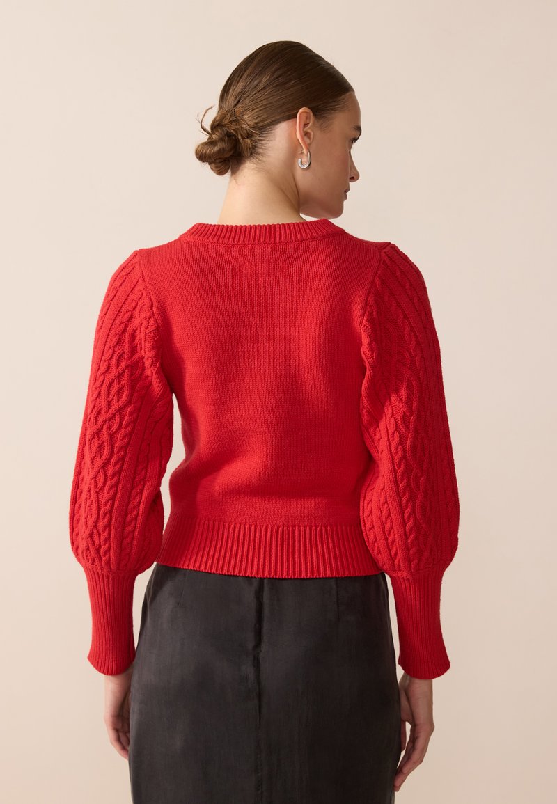 Czerwony sweter z dzianiny, z kablowym wzorem, bufkami na rękawach i prążkowanym wykończeniem. Widok z tyłu pokazuje okrągły dekolt i teksturowane detale.
