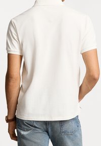 Vit polo skjorta med texturerat tyg, korta ärmar och ribbad krage. Matchad med ljusblå jeans, visande bakvy.