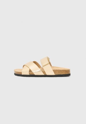 Beige lædersandaler med tværgående stropper og justerbar Velcro-lukning, korksål og sort gummisål. Glat tekstur, minimalistisk design.