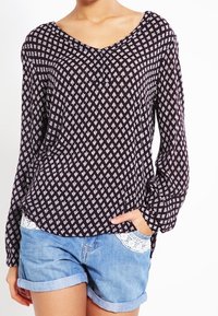 Dunkel gemusterte Bluse mit V-Ausschnitt und langen Ärmeln, die ein geometrisches Design in Weiß und Hellgrau auf einem navyblauen Hintergrund zeigt.