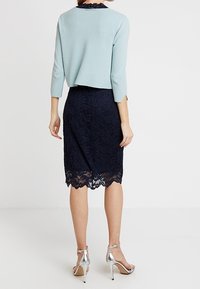 Helle blaue, kurz geschnittene Strickjacke mit drei Viertelärmeln, kombiniert mit einem navyfarbenen Bleistiftrock aus Spitze mit gewelltem Saum und silbernen High Heels.