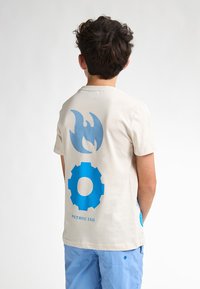 Camiseta de manga corta color beige claro con diseños gráficos azules: una llama, un engranaje y el texto impreso "PETROL' IND." Textura de algodón suave.