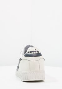 Vita lädersneaker med grå detaljer, texturerad häl, gummisula och logotyp på bakre hälen. Enkel design med låg profil.