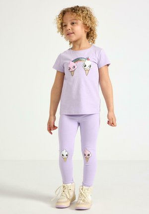 Lille barn med krøllet hår iført matchende lavendel top og leggings, begge med smilende isvaffeldesigns og en regnbue detalje.