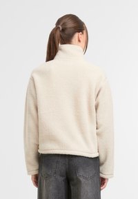 Jasno beżowy polarowy sweter z wysokim kołnierzem, teksturowany materiał i krótki fason, w połączeniu z ciemnoszarymi szerokimi spodniami.