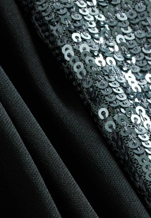 Un tissu noir drape sur un fond d'ornement en sequins argentés, mettant en valeur un contraste texturé entre des surfaces lisses et brillantes.