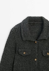 Dunkelgraue Strickjacke mit weitem Kragen, zwei Brusttaschen und goldfarbenen Knopfakzenten. Strukturierter Stoff mit grobem Strickmuster.