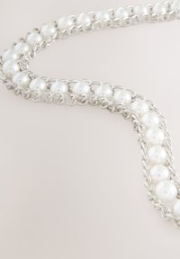 Collana con catenina d'argento con perle bianche, disposte in un anello continuo con un design a maglie testurizzate e superfici lisce delle perle.