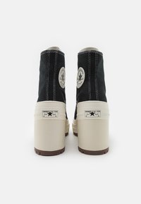 Black canvas ankle boots with white stitching, featuring iconic circular patches and cream platform soles with brown rubber bottoms.