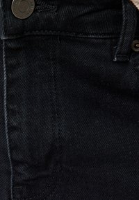 Tela de mezclilla negra con una textura suave, que presenta un bolsillo frontal, costuras en contraste y un detalle de botón de metal negro.