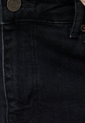 Sort denimstof med en glat tekstur, der har en frontlomme, kontrasterende syninger og en detalje med en sort metalknap.