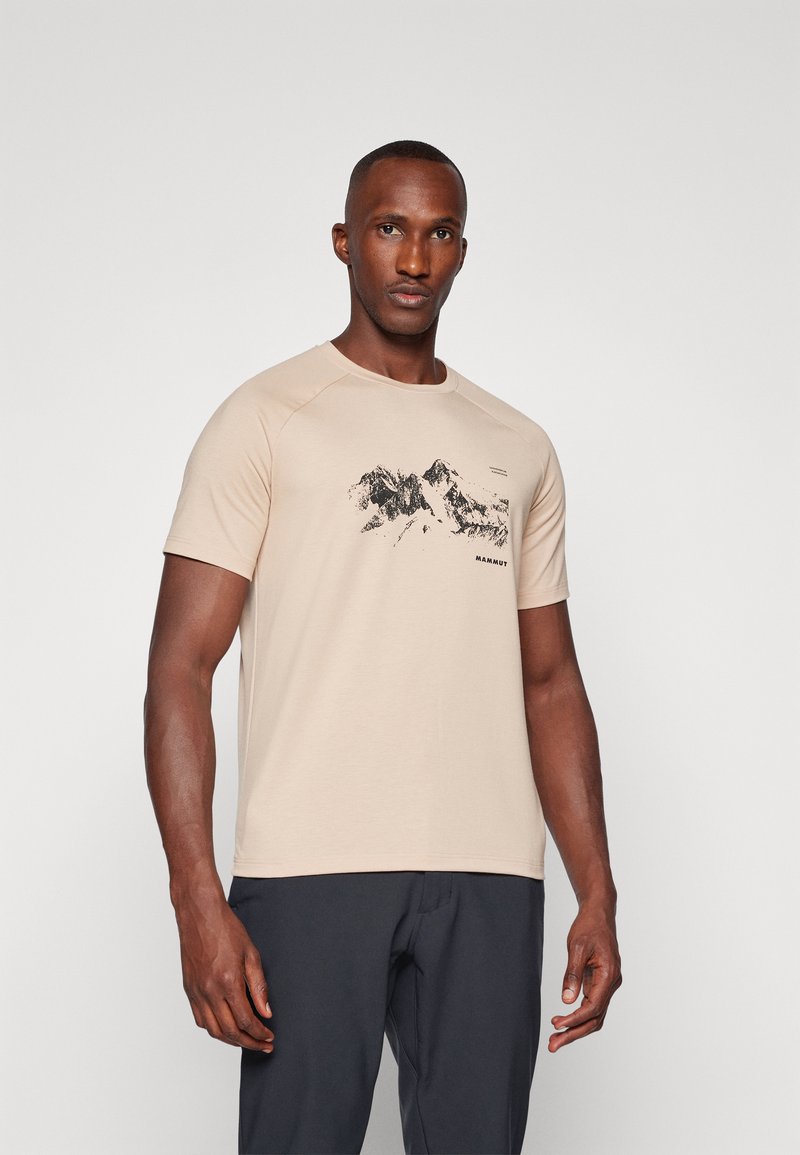 Beżowa koszulka z krótkim rękawem z miękkiego materiału z czarną grafiką górską i logo "MAMMUT" pod wzorem. Klasyczny krój z okrągłym dekoltem.