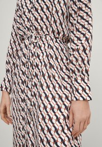 Knielanges Hemdkleid mit geometrischem Muster in Marineblau, Weiß und Rost; verfügt über lange Ärmel, einen Taillengurt und einen strukturierten Stoff.