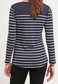 Woman wearing a navy blue long-sleeve shirt with white horizontal stripes, paired with black pants, shown from the back.