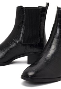 Botines negros con textura de cocodrilo, paneles laterales elásticos y un bajo tacón cuadrado. Acabado liso con diseño de puntera puntiaguda.