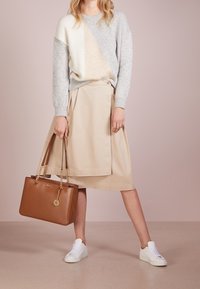Grijs en crèmekleurige color-block gebreide trui, beige wikkelsrok, witte sneakers en een bruine handtas met kettinghengsels en een logo-detail.
