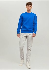 Sweatshirt de algodão azul com decote redondo, combinado com calças slim-fit cinza claro e ténis brancos. Textura suave, ajuste casual.
