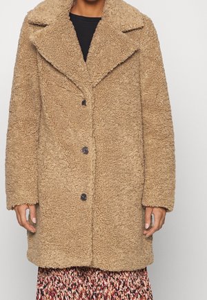 Ruskea, pörröinen, ylisuuri takki, jossa on tekstuuripinta, suuri kaulus ja kolme mustaa nappia. Vuoreksena kuvioitu hame.