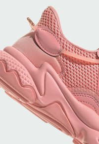 Scarpa atletica rosa con tessuto a rete e accenti sintetici lisci. Suola di gomma testurizzata con design ondulato. Dettagli cuciti evidenti.