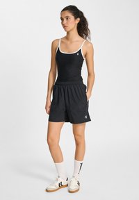 Svart atletisk linne med vita axelremmar, parat med svarta shorts med fickor. Tillbehören inkluderar vita strumpor och sneakers med svarta accenter.