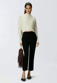 Kremeni skraćeni pulover, crne hlače visokog struka i smeđa torba sa resicama. Crne cipele s petom s dekorativnim akcentima.