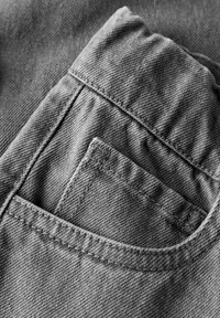 Close-up de dois bolsos de jeans, destacando a costura detalhada e a textura do tecido denim em escala de cinza.