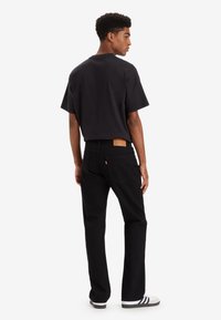 Zwarte t-shirt met korte mouwen gecombineerd met zwarte jeans, voorzien van een leren patch op de tailleband en gestreepte zwart-witte sneakers.