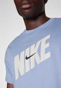 Camiseta de algodón azul claro con un gran logo de Nike en blanco y un swoosh negro. Diseño de mangas cortas y cuello redondo.