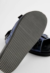 Sorte sandaler med en blank marineblå overdækning, der har en robust gummisål med vandrette riller for godt greb og en spænde detalje.