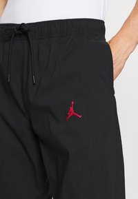 Schwarze Shorts mit elastischem Bund und Zugband, mit einem roten gestickten Jumpman-Logo am linken Bein. Glatte Stofftextur.