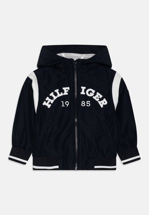 Czarna kurtka z kapturem i suwakiem, białe paski na rękawach i mankietach, napis "HILFIGER 1985" z przodu, dwie przednie kieszenie oraz elastyczny ściągacz.