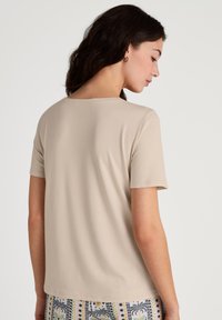 T-shirt beige a maniche corte con scollatura rotonda e texture liscia. Stilizzato con tessuto decorato sul fondo, che mostra un design variegato.