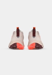 Rear view of athletic shoes featuring a light pink mesh upper, orange accents, and a textured rubber sole with bright orange details.