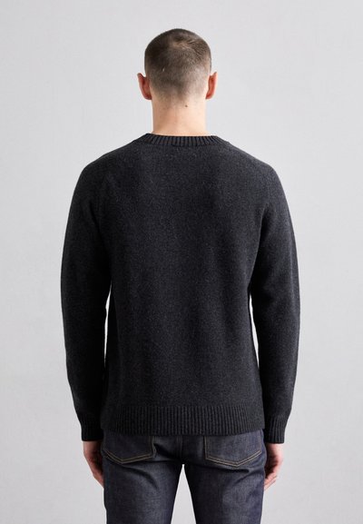 Mørk grå strikkegenser med rund hals og ribbestrikkede mansjetter og hem, med en strukturell finish. Brukt over mørke jeans.