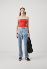 Rdeč brezramni top, svetlo modri široki jeans s podrobno šivanje. Črna pregibna torba in temni športni copati z belimi črtami dopolnjujejo videz.