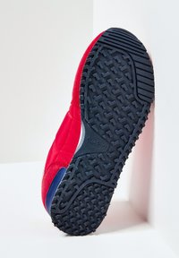 Sneaker rossa con tomaia in camoscio e tessuto; suola in gomma con motivo a zigzag; accent blu vicino al tallone; logo impresso di lato.