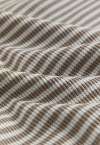 Geweven stof met afwisselende strepen in bruin en wit. Zachte textuur met een subtiel ribbelpatroon, met zachte plooien en krommingen.