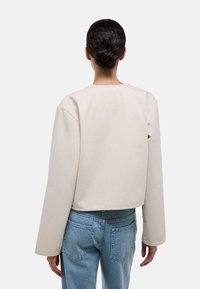 Sweatshirt court beige clair à manches longues, fabriqué en tissu coton doux. Présente un col rond et des lignes simples et épurées.