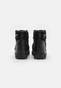 Botas Sorel negras con parte superior de ante y piel sintética, diseño redondeado y suela de goma texturizada. Logo grabado en el talón y en la parte posterior.