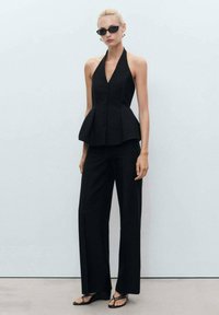 Černý halter krk peplum top s knoflíky v kombinaci s kalhotami širokého střihu a plochými sandály. Hladká tkanina, minimalistický design, bez vzorů.