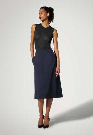 Combinaison sans manches noire associée à une jupe midi évasée bleu marine avec poches latérales, texture lisse et talons hauts.