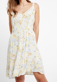 Blommig klänning med ett mönster i gult, blått och vitt, V-ringning, tunna band och en utsvängd kjol med rynkad midja. Bomullstyg.