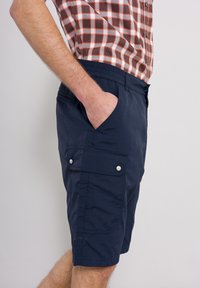 Marina cargo shorts med sidofickor, elastisk midja och tryckknappdetaljer; tillverkade av lätt material med texturerad yta.