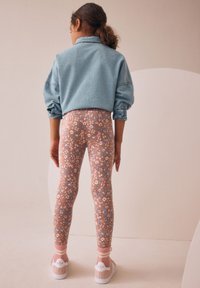 Denimjakke med op rullede ærmer, blomstrede leggings i pastelfarver og lyse sneakers med et karakteristisk logo samt stribede sokker.